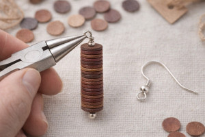 Hand holding pliers while attaching a hook to a leather disc earring