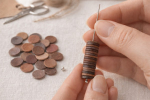 Hands threading brown-toned leather discs onto a needle during earring production